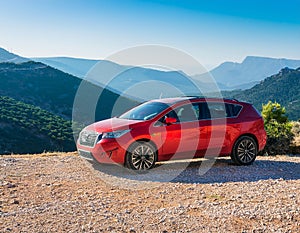 A new red car pulled over on the side of a remote mountain road