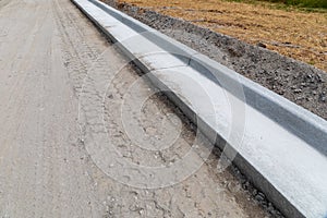 New road under construction, dirt roadway edged with freshly formed concrete curbing, copy space