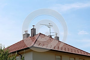 New roof tiles with modern chimneys and multiple TV antennas on top of renovated suburban family house