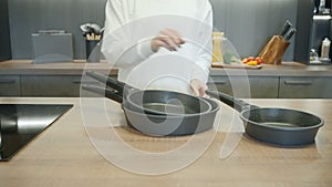 New set of frying pans demonstrated by a chef in white uniform. Action. Interior of a modern kitchen.