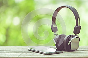 New smartphone and headphone on wooden table with green space nature blur background