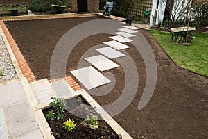New stepping stone slabs along a landscaped garden with soil prepared ready for ne grass turf lawn to be installed