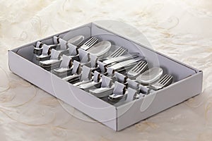 New from the store, spoons, forks, knives, cake forks and teaspoons in a box, on table with white tablecloth