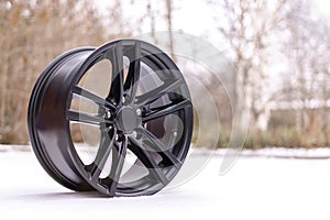 New stylish black brushed aluminum alloy wheel, on white snow. Winter. auto tune up services