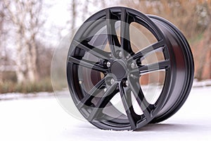 New stylish black brushed aluminum alloy wheel, on white snow. Winter. close up.