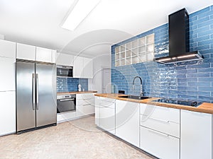 New stylish bright kitchen with white cabinets and blue tiles. Spacious modern fully equipped appliance interior with wooden desk