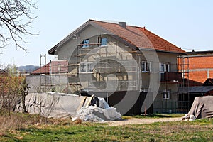 New suburban family house under construction surrounded with building scaffolding and other houses next to temporary flood