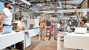 New team member. Young man in casual wear holding box with things while his new coworkers greeting him in the modern