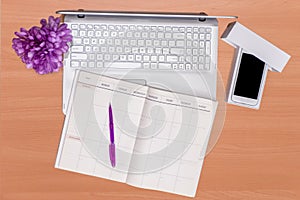 New technology on desk: open laptop, unboxed mobile phone and open notebook with purple pen and flowers