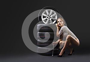 New tires stack and beautiful girl with wrench on a dark background.