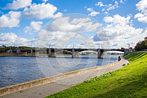 The new Volga bridge and city quay in Tver, Russia. Picturesque river landscape. Clouds in the blue sky. Green grass on the lawn