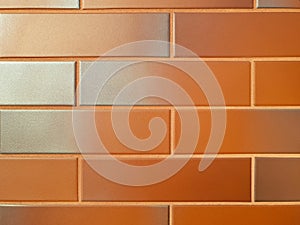 New wall tiled bright orange bricks with a silvery gray shade, shining in the sun. Modern facade.