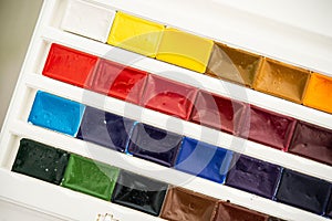 New watercolor paints  in cuvettes in a white plastic box with a palette