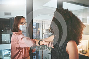 The new way to shake hands. two businesswomen standing together and elbowing each other and wearing face masks during a
