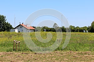 New weather station building surrounded with various weather instruments housed in protective boxes and tall grass