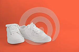 New white female or teen sneakers isolated on coral background. White textile sneakers with rubber soles with tied laces on a