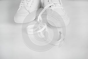 New white female or teen textile sneakers isolated on white background. White rubber-sneakers with untied laces on a light gray