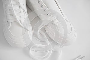 New white female or teen textile sneakers isolated on white background. White rubber-sneakers with untied laces on a light gray