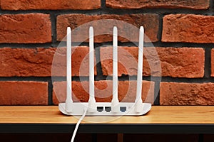 New white Wi-Fi router on wooden table near brick wall