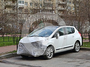A new white wrecked car after an accident is covered with plastic wrap