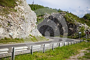 A new winding asphalt black road with a white dividing strip and safe fance between the rocks in the Altai mountains under a clear