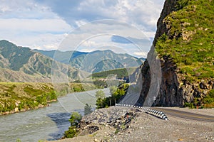 A new winding asphalt black road with a yellow dividing strip between the rocks and the Katun River in the Altai mountains under a