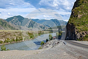 A new winding asphalt black road with a yellow dividing strip between the rocks and the Katun River in the Altai mountains under a