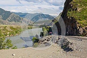 A new winding asphalt black road with a yellow dividing strip between the rocks and the Katun River in the Altai mountains under a