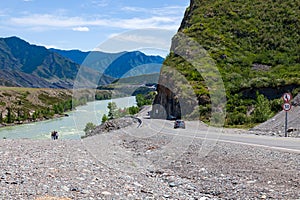 A new winding asphalt black road with a yellow dividing strip between the rocks and the Katun River in the Altai mountains under a
