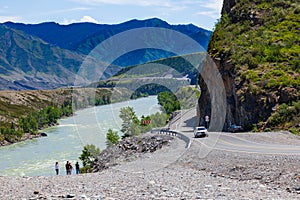 A new winding asphalt black road with a yellow dividing strip between the rocks and the Katun River in the Altai mountains under a