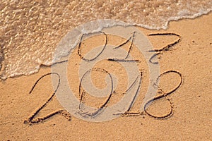New Year 2018 is coming concept - inscription 2017 and 2018 on a beach sand, the wave is almost covering the digits 2017