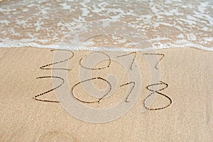 New Year 2018 is coming concept - inscription 2017 and 2018 on a beach sand, the wave is almost covering the digits 2017