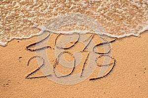 New Year 2019 is coming concept - inscription 2018 and 2019 on a beach sand, the wave is almost covering the digits 2018