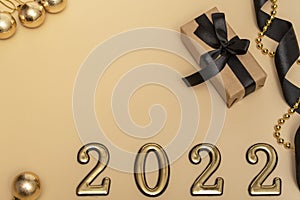 New Year 2022. Top view New Year mockup on beige background: black ribbon, gift box, golden numbers and multicolored sparkles.