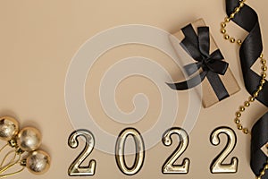 New Year 2022. Top view New Year mockup on beige background: black ribbon, gift box, golden numbers and multicolored sparkles.