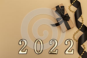 New Year 2022. Top view New Year mockup on beige background: black ribbon, gift box, golden numbers and multicolored sparkles.