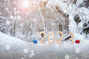 New year 2023 wooden digits in a snowdrift in sunny winter forest with Christmas balls