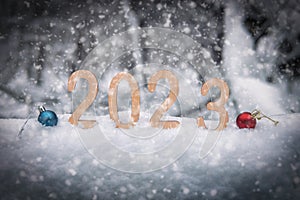 New year 2023 wooden digits in a snowdrift in winter forest in twilight with Christmas balls