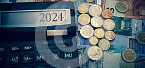 New Year 2024. Calculator with the number 2024 on the screen against the background of euro coins and banknotes