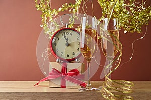 New Year 2024 celebration festive background with champagne glasses, gift box and clock on wooden table over golden decorations