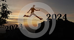 new year 2024 concept with Abstract silhouette man jumping on top of mountain from 2023 text to 2024