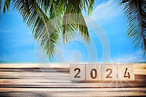 New year 2024 on wooden cube and stack of coins on planks on tropical beach background