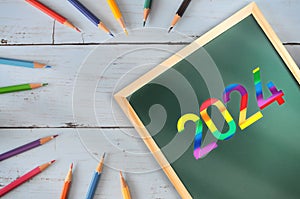 New year 2024 written on chalkboard with colored pencil on wooden desk