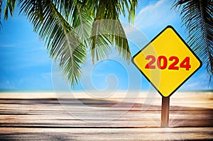 New year 2024 written on yellow sign on plank and beach background