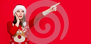 New year advertising. Christmas woman pointing finger away at copy space. Surprised girl in Santa hat. Season Sales and