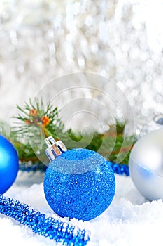 New Year background with blue and silver Christmas balls in snow, spruce green branches on light background.