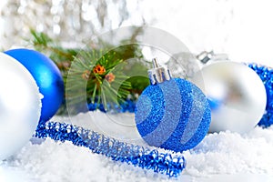New Year background with blue and silver Christmas balls in snow, spruce green branches on light background.