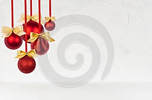 New Year background in simple style with shiny red balls with golden bows hanging on ribbon as bunch on soft light white wall.