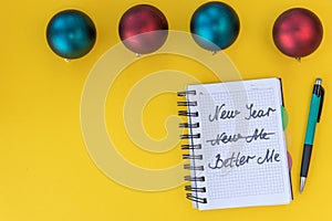 New year, better me. Happy new year quote. Writing in a notebook New year, better me on yellow background with Christmas balls.