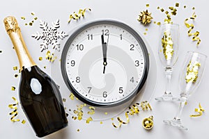 New year celebration concept with a bottle of champagne and two glasses toasting. Christmas gift box, alarm clock and